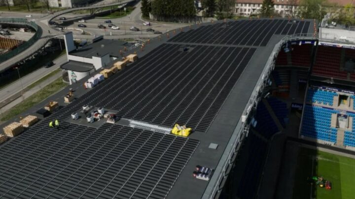  Online Backup: Aerial view of a large building with solar panels installed on the roof. Adjacent to the building, there is a seating area resembling a sports stadium, suggesting that the building may be part of a sports complex or similar facility. The presence of solar panels indicates a focus on sustainable energy practices, which could be relevant for discussions about renewable energy solutions in urban or communal spaces